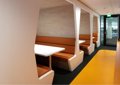 Moderne zithoeken met oranje banken en witte tafels in een kantoor aan de Karel Doormanweg.